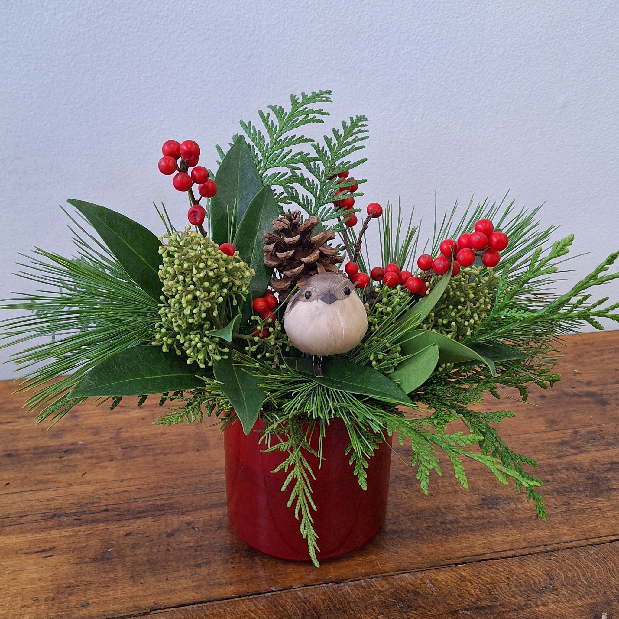 Decorative Christmas arrangement with greenery, berries, and pinecones on a wooden surface.